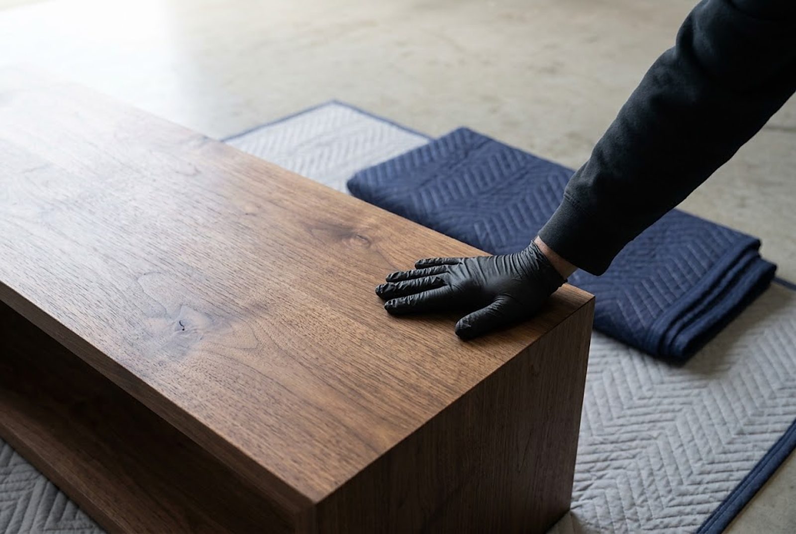 A gloved hand checking the surface of a walnut table top on a padded bench