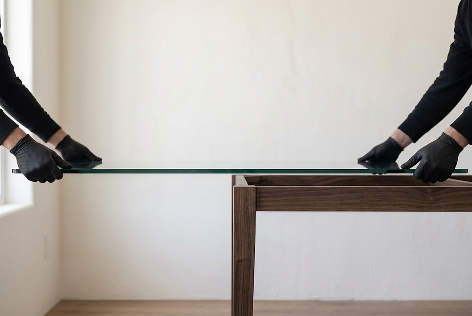 Two installers in gloves lowering a glass top onto a walnut table base