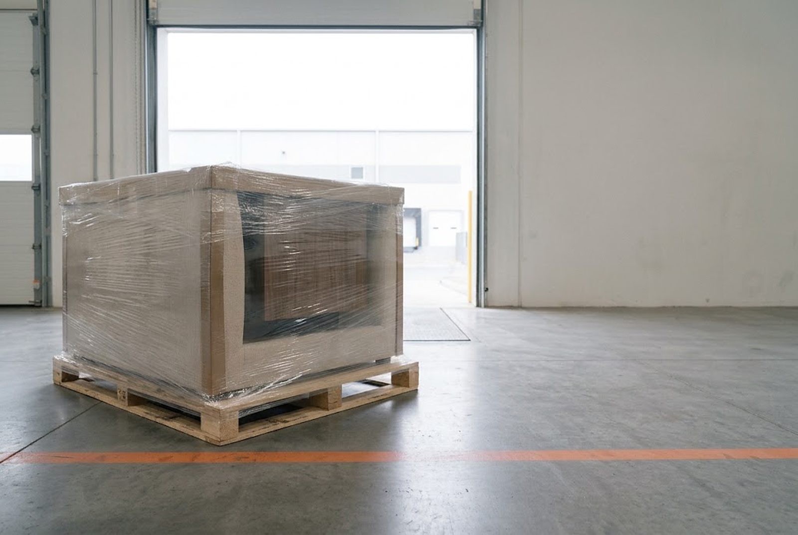 A shrink-wrapped pallet of furniture standing inside an open warehouse dock door